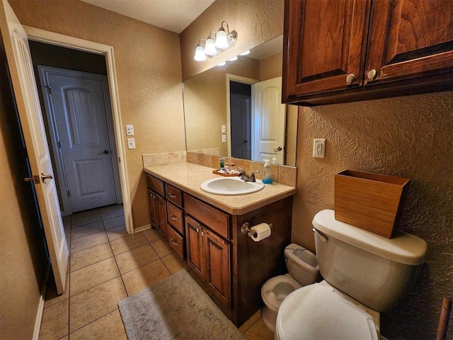bathroom featuring toilet, a textured wall, vanity, and tile patterned floors