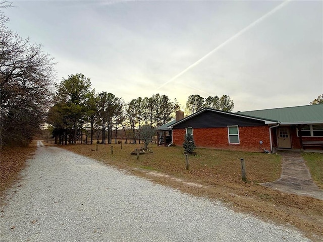 view of front facade with gravel driveway, brick siding, and a chimney