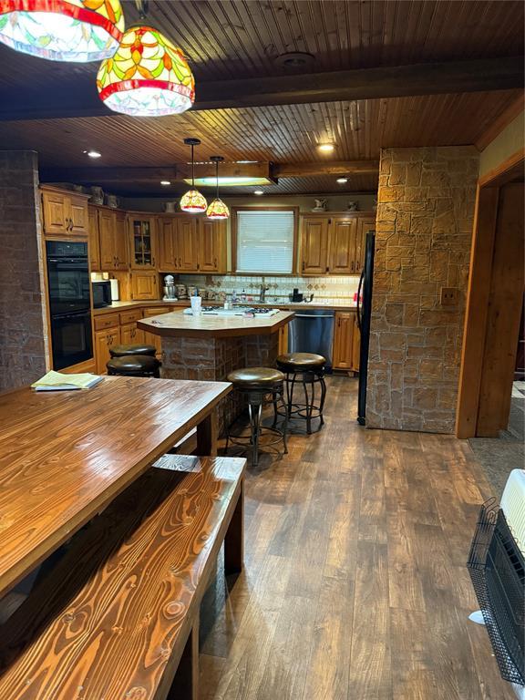 kitchen with a center island, dark wood finished floors, beamed ceiling, brown cabinetry, and black appliances
