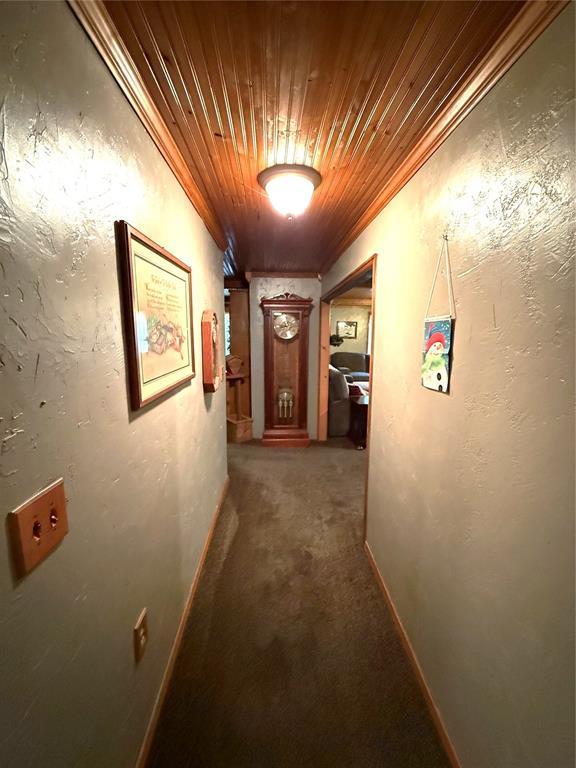 corridor featuring a textured wall, wood ceiling, baseboards, and carpet floors