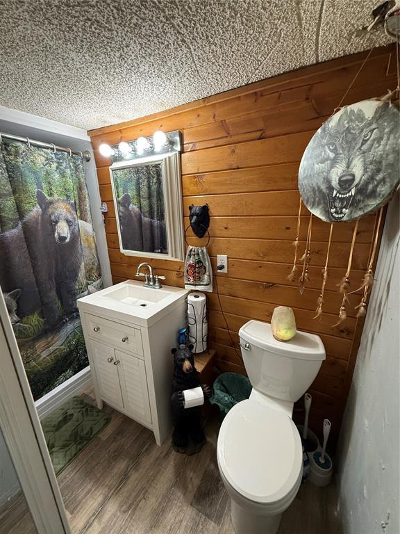 full bath with vanity, wooden walls, a shower with curtain, and wood finished floors