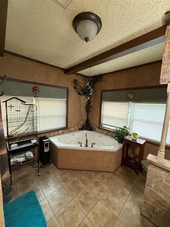 full bathroom featuring tile patterned flooring, beamed ceiling, a bath, and a textured ceiling