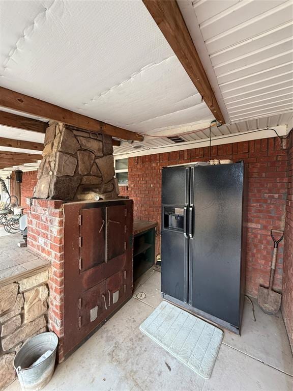 below grade area with brick wall and black refrigerator with ice dispenser