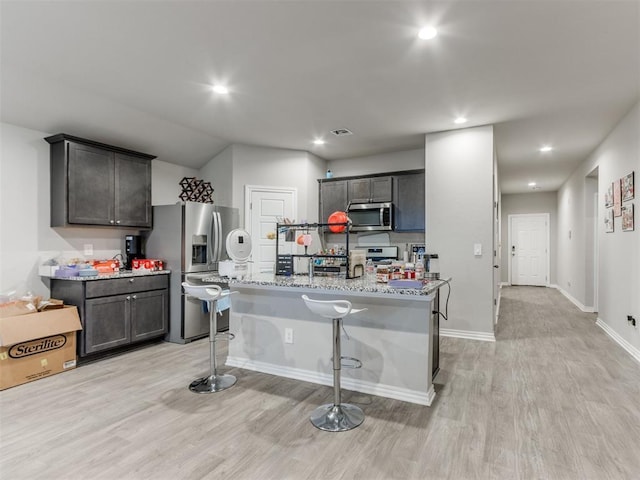 4408 Moonlight Rd, Mustang, OK 73064 - kitchen with appliances with stainless steel finishes, light wood-style floors, light stone countertops, a kitchen island with sink, and recessed lighting