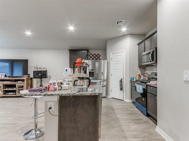 kitchen featuring light stone countertops, stainless steel appliances, light hardwood / wood-style flooring, a kitchen bar, and a kitchen island with sink