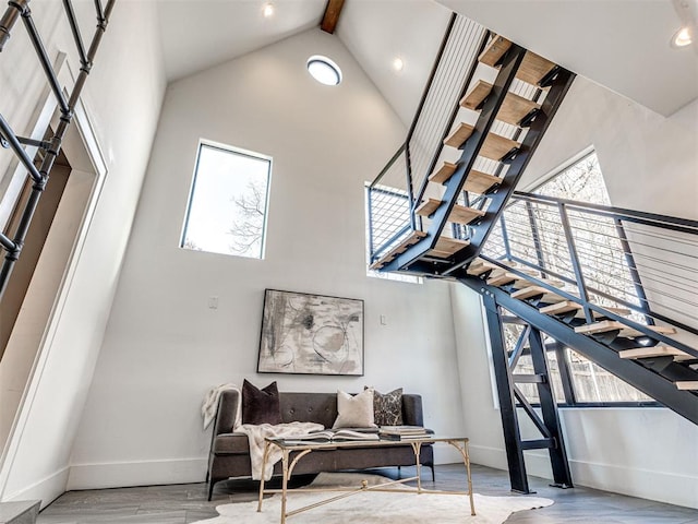 stairs featuring beamed ceiling, wood-type flooring, and high vaulted ceiling