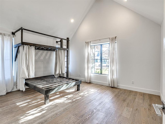 unfurnished bedroom with high vaulted ceiling and light wood-type flooring