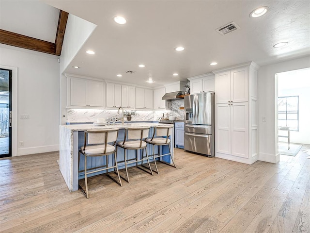 kitchen featuring a breakfast bar, backsplash, an island with sink, white cabinets, and stainless steel fridge with ice dispenser