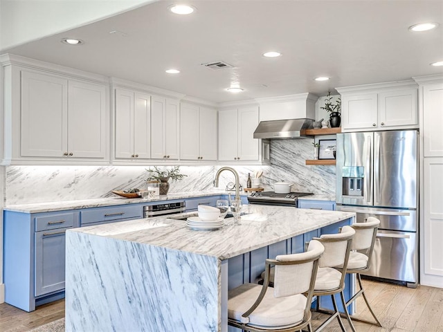 kitchen with stainless steel appliances, white cabinetry, a center island with sink, and wall chimney range hood