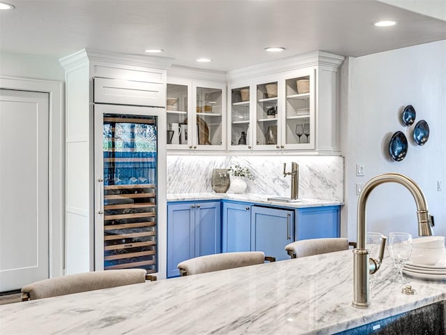 bar with blue cabinetry, white cabinetry, light stone counters, beverage cooler, and decorative backsplash