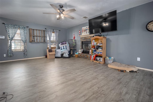 interior space featuring hardwood / wood-style flooring, a stone fireplace, ceiling fan, and a healthy amount of sunlight