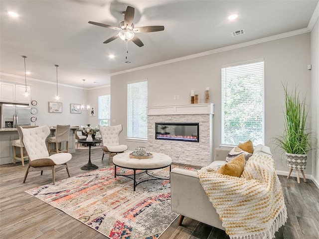 living room with a stone fireplace, ceiling fan, ornamental molding, and hardwood / wood-style flooring