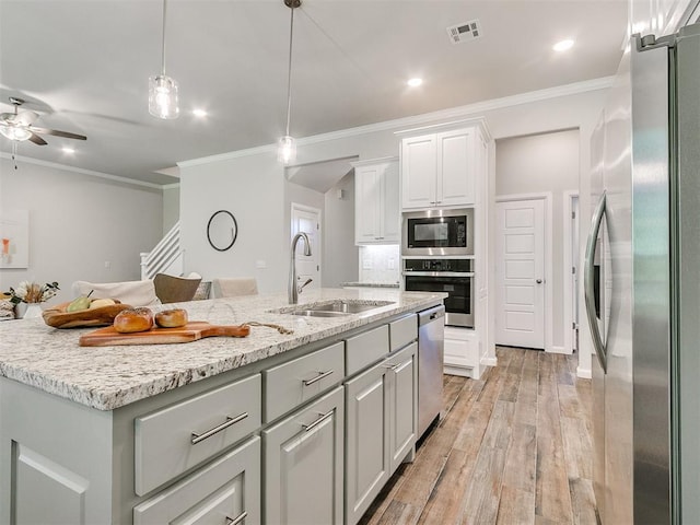 kitchen with pendant lighting, light wood-type flooring, an island with sink, white cabinetry, and stainless steel appliances