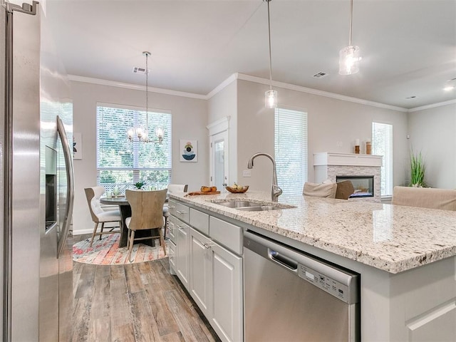 kitchen featuring appliances with stainless steel finishes, light wood-type flooring, sink, white cabinetry, and an island with sink