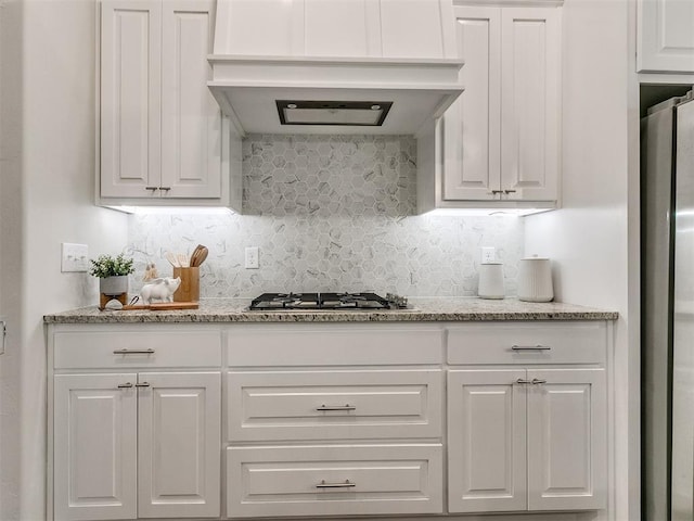 kitchen featuring white cabinetry, light stone countertops, stainless steel appliances, premium range hood, and decorative backsplash