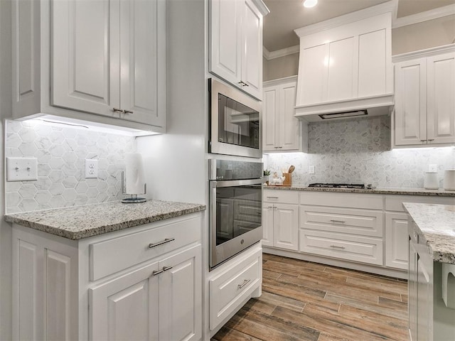 kitchen featuring crown molding, decorative backsplash, light wood-type flooring, white cabinetry, and stainless steel appliances