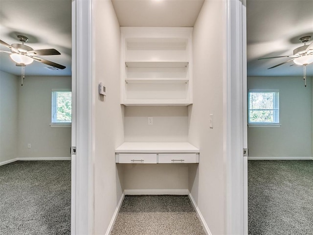 unfurnished office featuring carpet flooring, built in desk, and ceiling fan