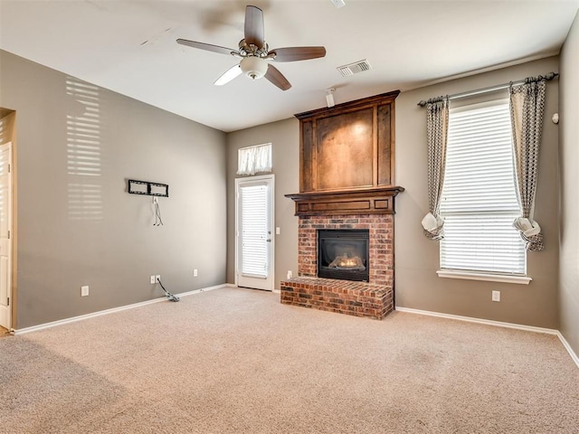 unfurnished living room featuring ceiling fan, plenty of natural light, light colored carpet, and a fireplace