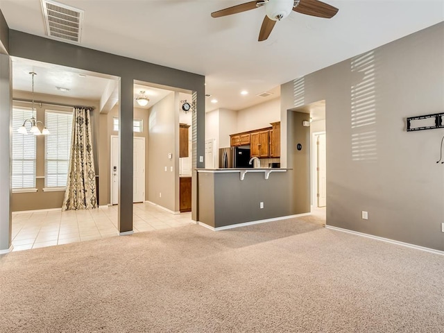 unfurnished living room with light colored carpet and ceiling fan with notable chandelier