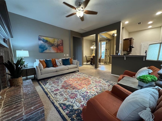 living room with ceiling fan with notable chandelier and a fireplace