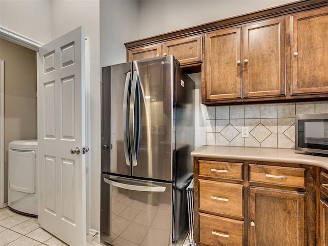 kitchen with stainless steel appliances, light tile patterned flooring, washer / dryer, and tasteful backsplash