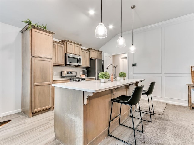 kitchen with light brown cabinets, a center island with sink, vaulted ceiling, appliances with stainless steel finishes, and decorative light fixtures