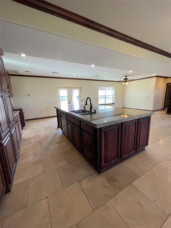 kitchen featuring dark stone counters, a sink, french doors, a center island with sink, and ornamental molding