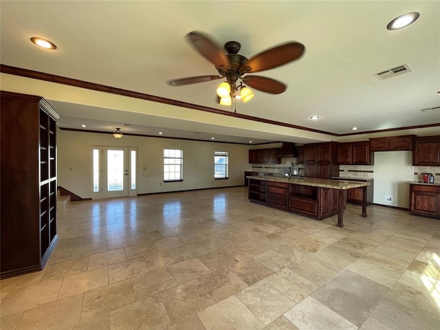kitchen with stone tile floors, range hood, visible vents, crown molding, and ceiling fan