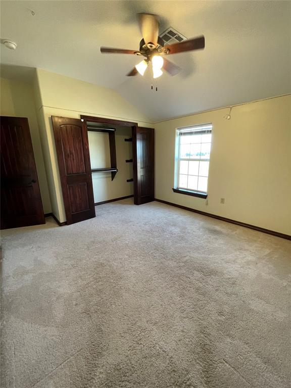unfurnished bedroom featuring lofted ceiling, visible vents, baseboards, and light carpet
