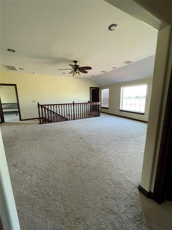 carpeted empty room featuring baseboards, vaulted ceiling, visible vents, and ceiling fan
