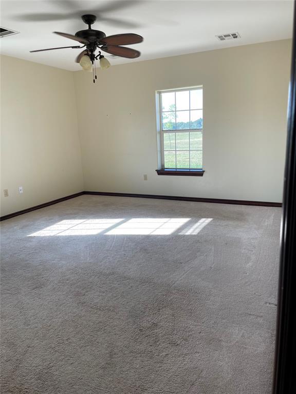 carpeted empty room featuring baseboards, a ceiling fan, and visible vents