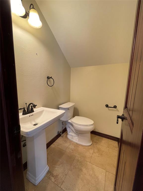 half bath with toilet, tile patterned floors, a sink, baseboards, and lofted ceiling