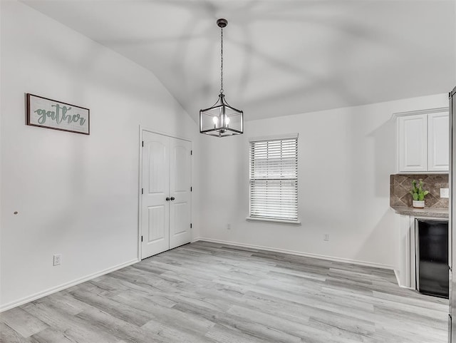 unfurnished dining area with lofted ceiling, a notable chandelier, and light hardwood / wood-style floors