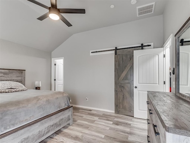 bedroom with vaulted ceiling, a barn door, ceiling fan, and light hardwood / wood-style floors