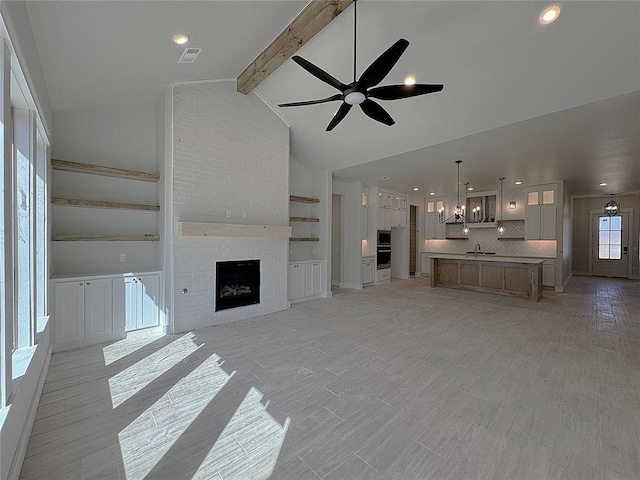 unfurnished living room with visible vents, vaulted ceiling with beams, a fireplace, a sink, and ceiling fan with notable chandelier