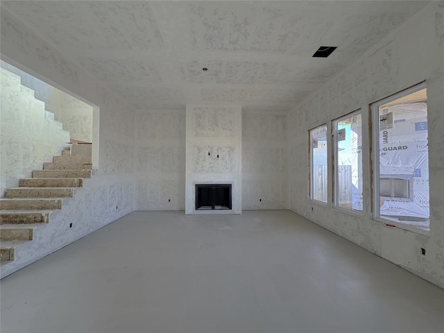 unfurnished living room with concrete flooring, a fireplace, and stairs