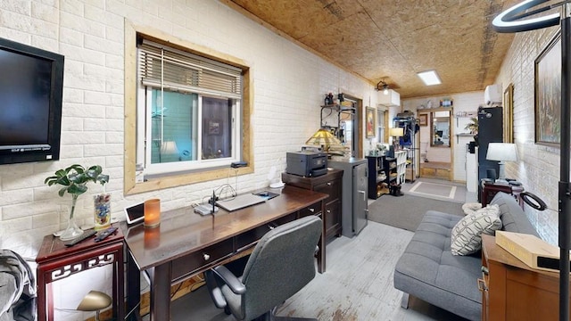 home office with light hardwood / wood-style flooring and brick wall