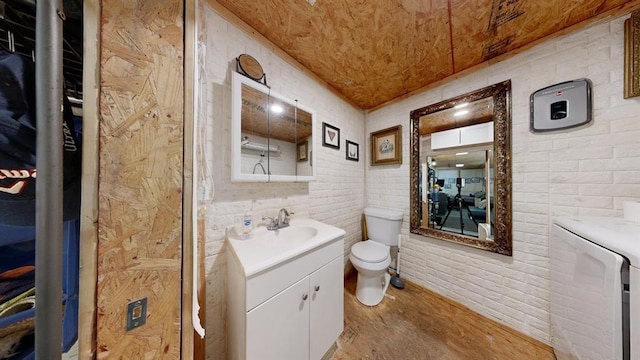 bathroom with hardwood / wood-style floors, vanity, toilet, independent washer and dryer, and brick wall