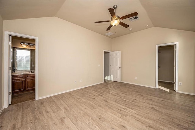 unfurnished bedroom featuring connected bathroom, a spacious closet, lofted ceiling, and light wood-type flooring