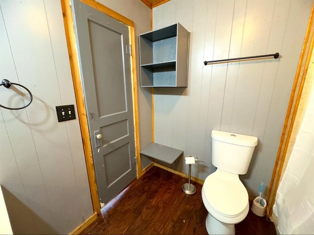 bathroom featuring toilet, wood walls, and hardwood / wood-style flooring