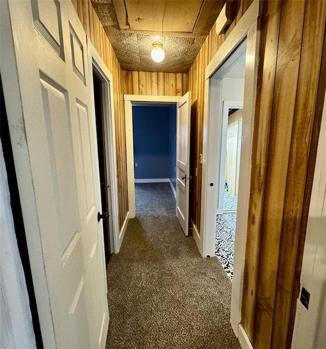 hallway featuring wooden walls and dark colored carpet