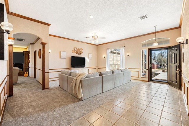 unfurnished living room with ceiling fan, ornamental molding, a textured ceiling, and light tile patterned floors