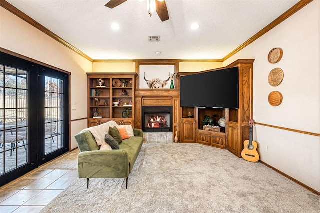 living room with a tile fireplace, crown molding, ceiling fan, a textured ceiling, and light colored carpet