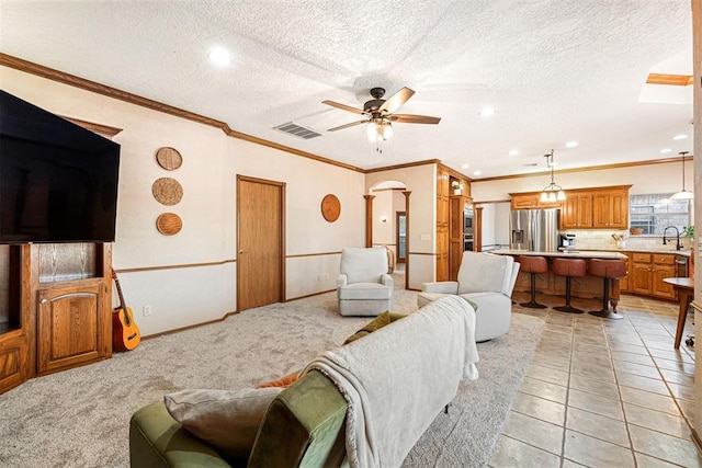 living room with sink, ceiling fan, ornamental molding, a textured ceiling, and light colored carpet