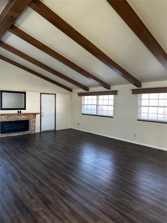 unfurnished living room with vaulted ceiling with beams, dark hardwood / wood-style floors, and a fireplace