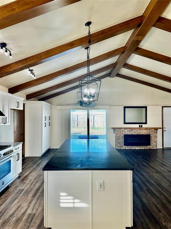 kitchen featuring vaulted ceiling with beams, white cabinets, high end stainless steel range oven, and a brick fireplace