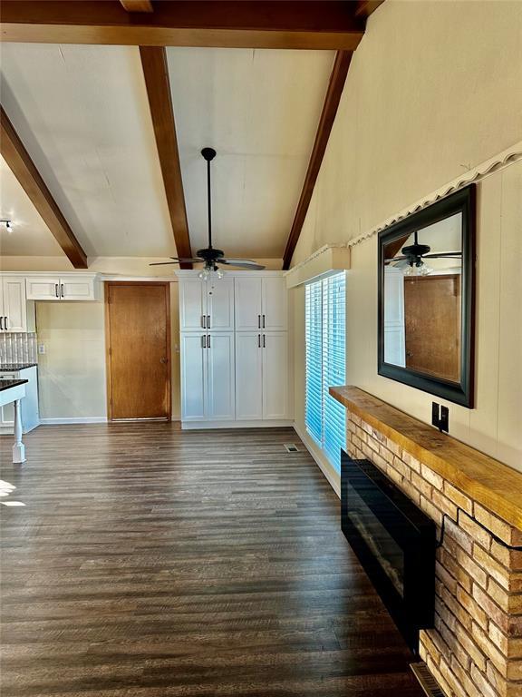 unfurnished living room with lofted ceiling with beams, a brick fireplace, ceiling fan, and dark wood-type flooring