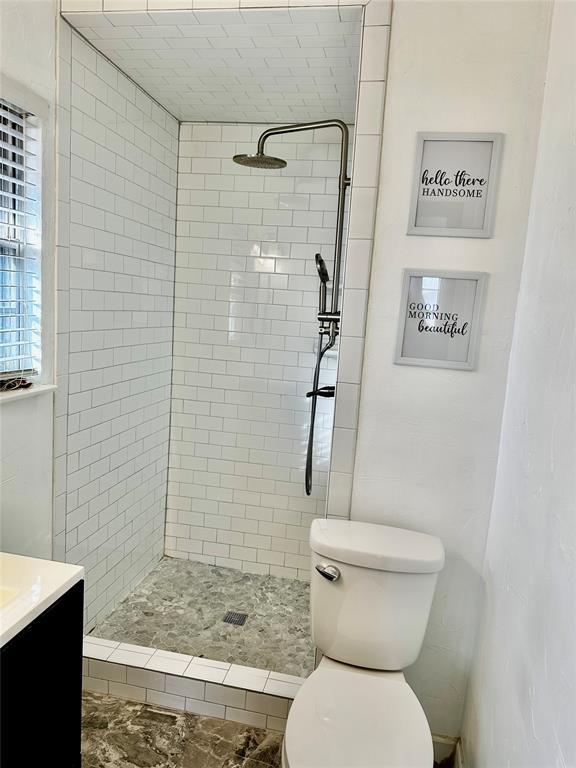 bathroom with a tile shower, vanity, and toilet