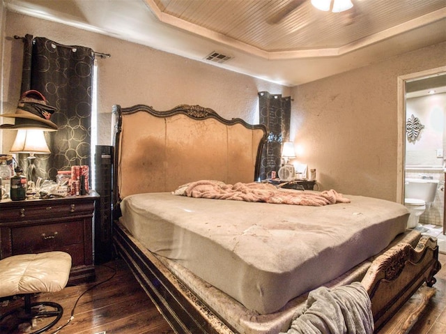 bedroom featuring hardwood / wood-style floors, a tray ceiling, ceiling fan, and ensuite bathroom