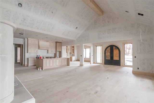 unfurnished living room featuring high vaulted ceiling, a healthy amount of sunlight, french doors, and light wood-type flooring